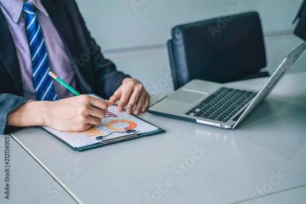 Fototapeta positive young business man sitting and working with documents and laptop,