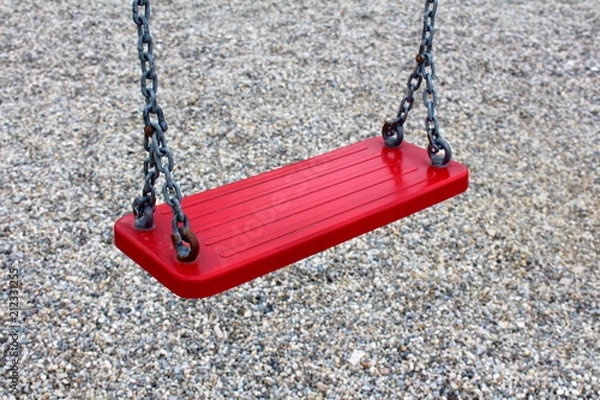 Fototapeta Outdoor public playground equipment metal swing red seat closeup with four holders tied with chain on playground sand background