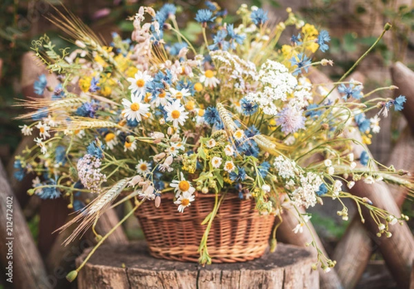 Fototapeta Wild flowers in a basket on a rustic background. Vintage scenery.