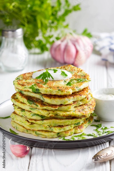 Obraz Zucchini pancakes with parsley and sour cream, summer food, tasty snack. High stack in a plate on white wood