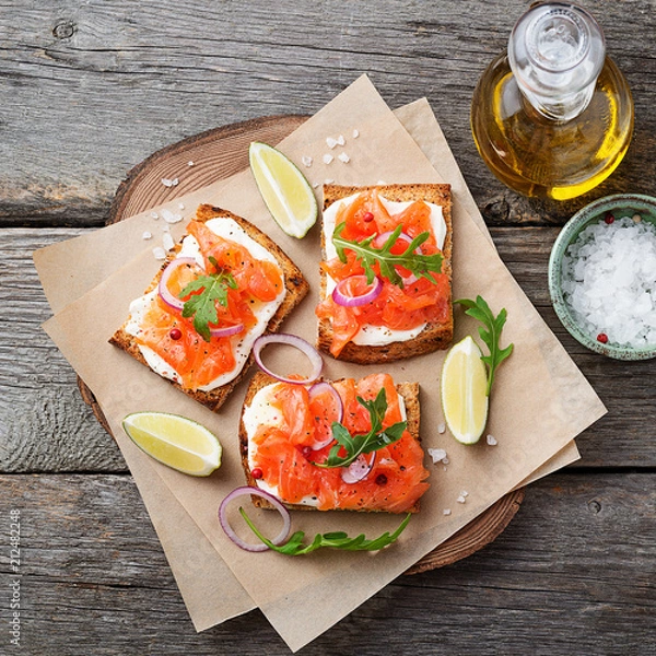 Fototapeta Smoked salmon sandwich with cream cheese on wooden table. top view