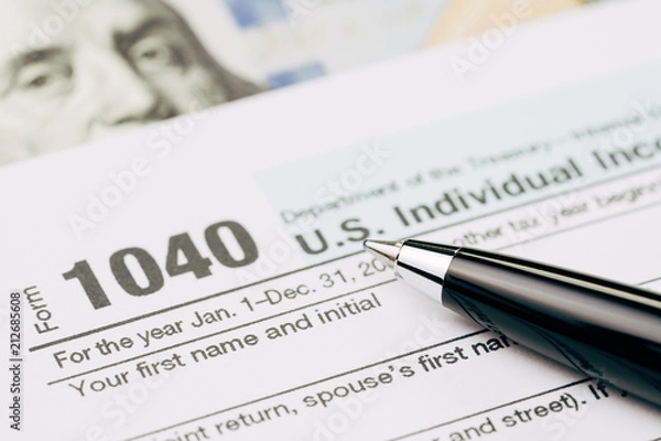 Fototapeta Tax time concept, selective focus on pen on 1040 US individual income tax filling form with US dollar bill, calculate from yearly revenue to pay the government
