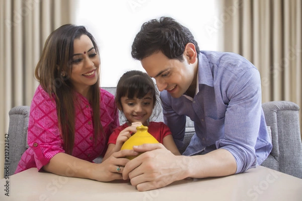 Fototapeta Parents and daughter saving money in clay piggy bank