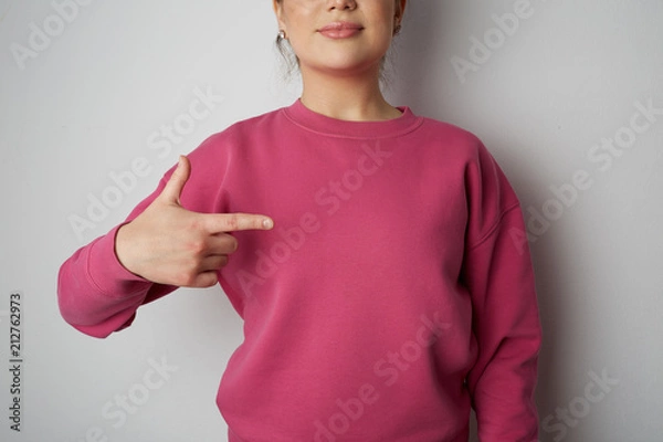Fototapeta Young hipster girl wearing pink hoody with space for your logo or design. Mock-up of pink hoody on gray empty wall in the background