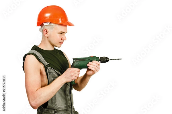 Fototapeta Young working guy in hard hat holds drill isolated on a white background