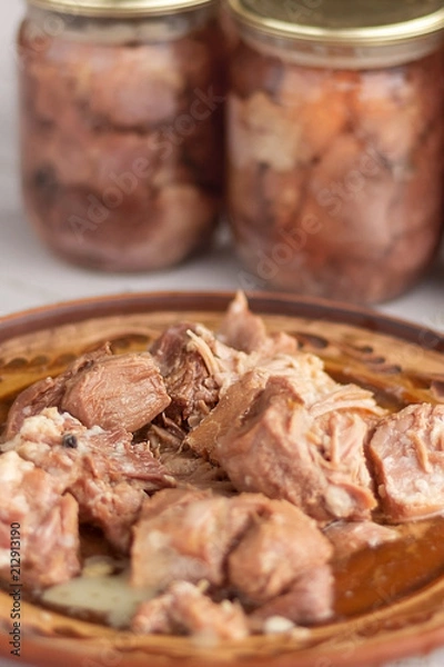Fototapeta pieces of stew meat on a clay plate on the background of glass cans with home preservation. Home cooking
