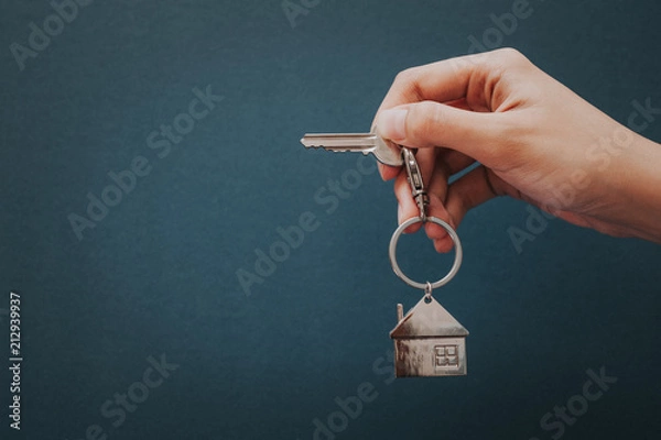 Fototapeta Woman's hand holding house key with house shape key chain.