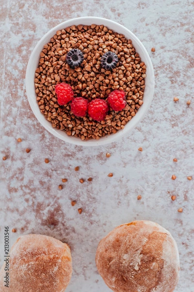 Obraz Smile from blackberries and raspberries in a plate with buckwheat and rolls.