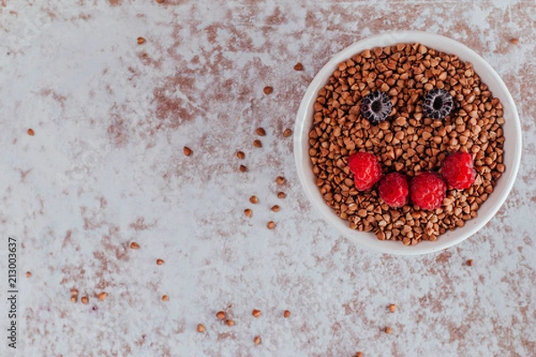 Obraz Smile from blackberries and raspberries in a plate with buckwheat and rolls.