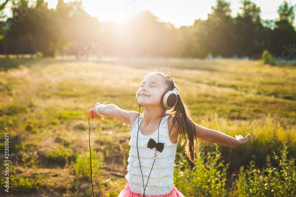 Obraz fine girl listening music with headphones and dancing, cute child enjoying music and resting