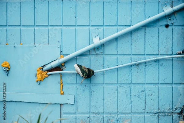 Fototapeta Blue wall from tiles with cyan closed hatchway and pipes close up. Background of wall of building with copy space.
