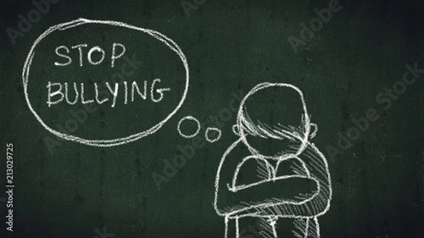 Fototapeta sad young boy sitting on the floor with text stop bullying written with chalk on chalkboard. social problems of humanity