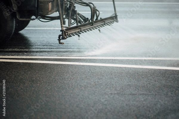 Fototapeta Cleaning sweeper machines washes the city asphalt road with water spray.