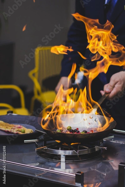 Fototapeta Chef doing flambe to food in pan with alcohol in big flame