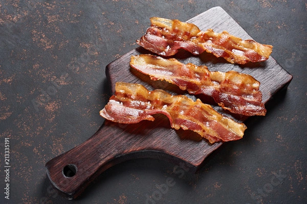 Fototapeta Fried bacon on wooden cutting board. Top view, isolated on black background.