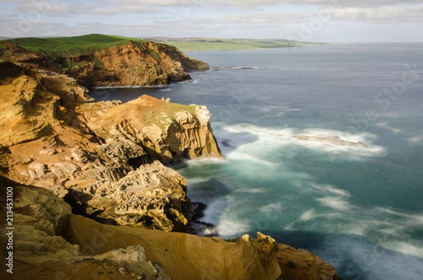 Fototapeta Elevated view of red sandstone cliffs illuminated by late afternoon light on the Chatham Islands, New Zealand. Long exposure.