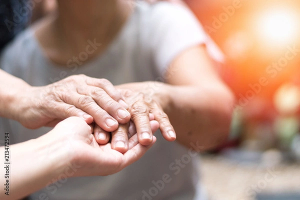 Fototapeta Caregiver, carer hand holding elder hand woman in hospice care. Philanthropy kindness to disabled concept.Public Service Recognition Week
