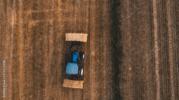 Fototapeta aerial view of harvest field with tractor moving hay bale around