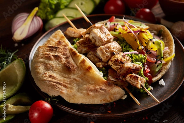 Fototapeta Exotic still slife with pita, fresh vegetables and kebab over wooden background, selective focus.