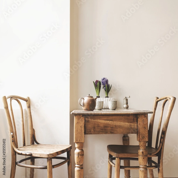 Fototapeta Vintage interior design of kitchen space with small table against white wall with simple chairs and plant decorations. Minimalistic concept of kitchen space.