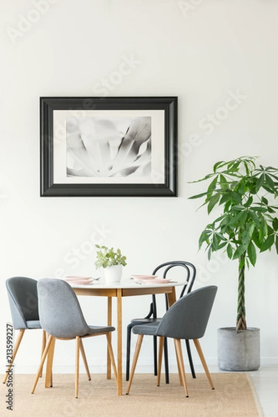 Fototapeta Real photo of a dining room interior with a table, chairs, tree and painting in a black frame