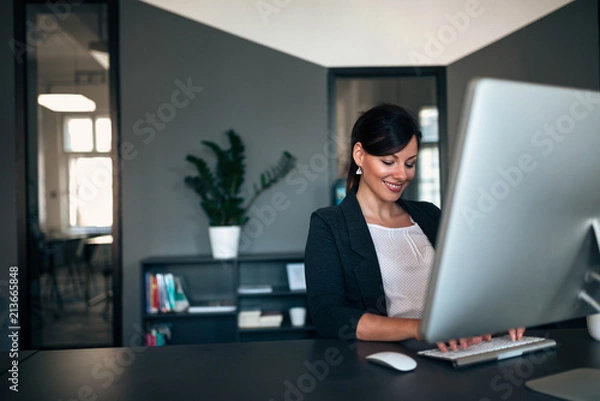 Fototapeta Female entrepreneur working while sitting at a desk typing on the computer keyboard.