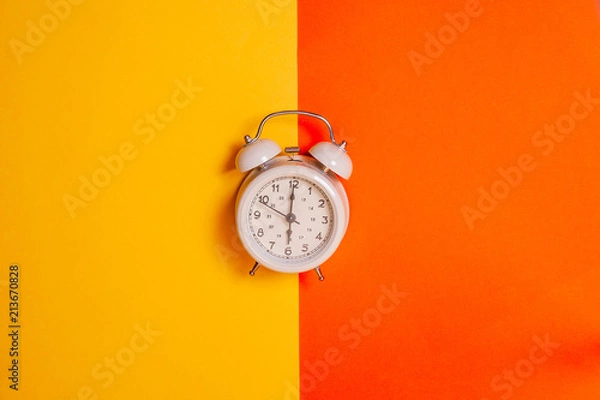 Fototapeta Vintage alarm clock on two tone solid color yellow and orange background. Early morning