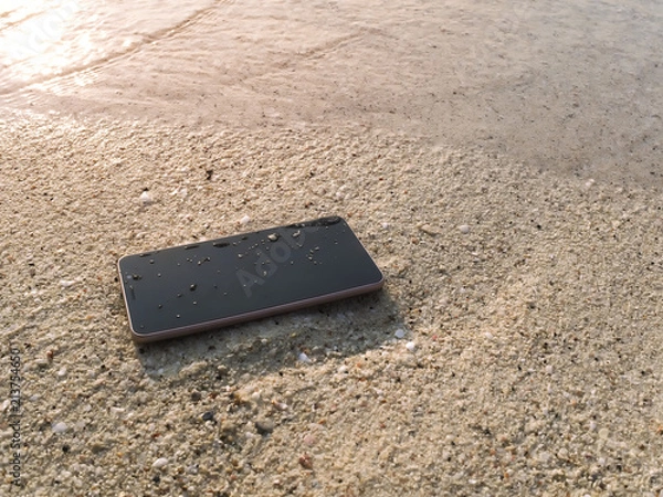 Fototapeta Mobile smart phone on the sandy beach with soft waves of sea background.  Internet of thing concept.