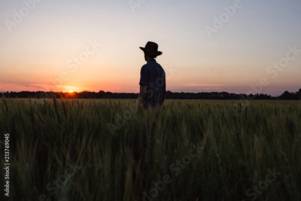 Fototapeta YOung male farmer stand alone in wheat field during sunset 