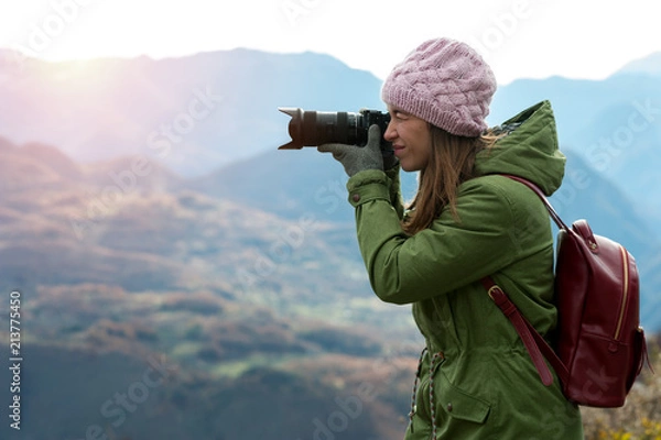 Fototapeta Charming young positive woman in autumn clothes with camera in hands while traveling through beautiful natural places. Concept of travel