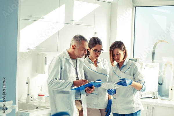 Fototapeta Medical dentist team in dental office discuss about practice and examining list of patients.