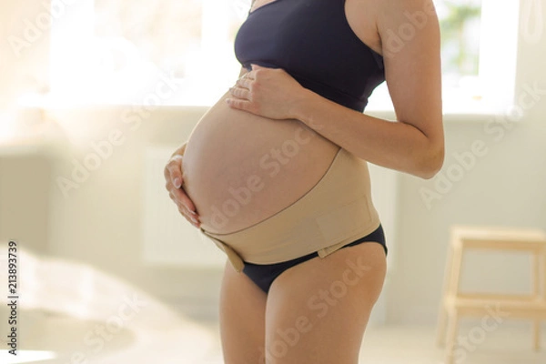 Obraz closeup belly of pregnant woman in bandage. Orthopedic abdominal support belt