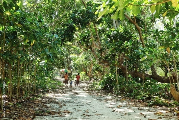 Obraz Lavatmangguemu, Pentecost Island / Vanuatu - APR 10 2016: woman walking home with kids on the sea shore path next to their village with an umbrella