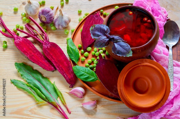 Obraz Homemade borscht with vegetables on the wooden background with fresh sliced beet, garlic, basil leaves and green peas. Traditional Ukrainian, Polish and Russian national beetrot soup. Top view