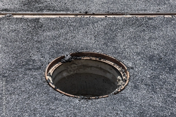 Fototapeta Głęboki właz bez przykrycia na jezdni podczas układania nowego asfaltu stanowi zagrożenie dla pieszych i samochodów