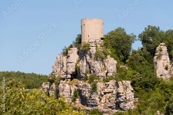 Fototapeta Alter runder Wachturm aus Naturstein auf einem Felsen vor blauem Himmel bei Balazuc