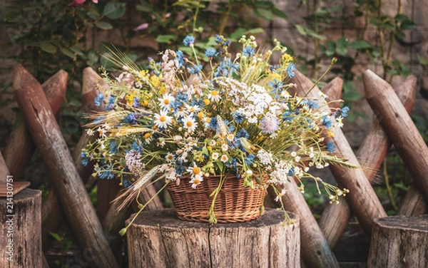 Fototapeta Wild flowers in a basket on a rustic background. Vintage scenery.