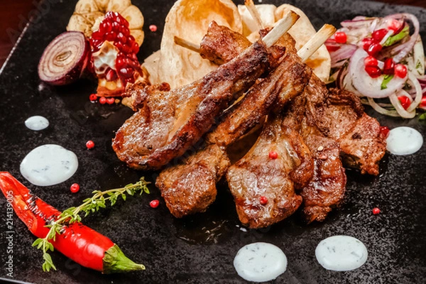 Fototapeta rack of lamb on a black plate decorated with pepper, pomegranate, onion and garlic