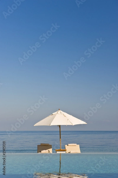 Fototapeta Deck chair and umbrella next to infinity pool