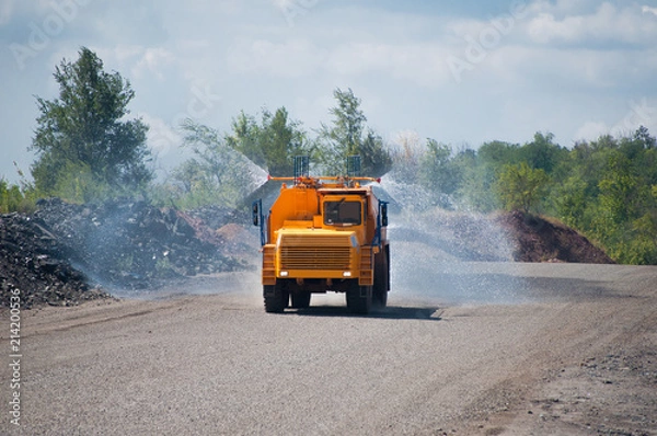 Obraz Heavy truck pours the road with water in the iron ore quarry. Dust removal, protection of the environment. Irrigation of the road from dust