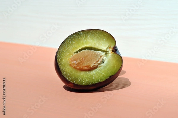 Fototapeta Half plum with a stone on a pink table