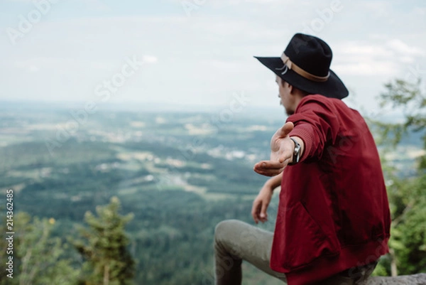 Fototapeta Man traveler sitting on a stone on the background of nature