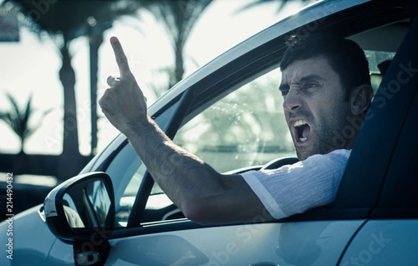 Fototapeta Furious man gesticulates with hand out of window while driving. Crazy driver yelling from car at sunrise. Stress, traffic rush hour, anxious, madness, rudeness concepts. Cold blue tone applied