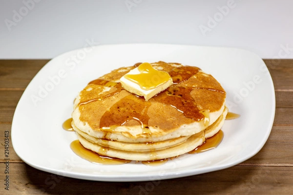 Fototapeta Pancake with a square of butter and syrup on a kitchen table waiting to be eaten
