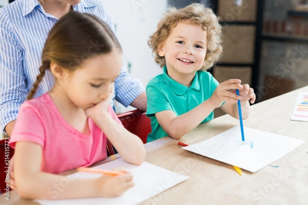 Obraz Smiling cute little boy drawing with color pencil together with girl at the table