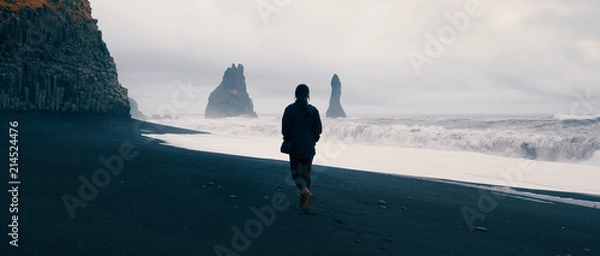 Fototapeta Kobieta idzie samotnie na czarnej plaży w Reynisfjara, Islandia.