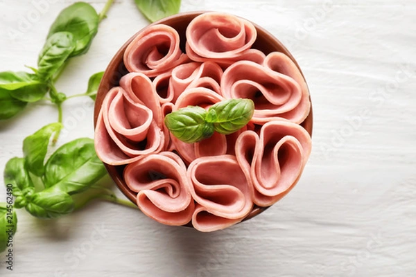 Fototapeta Bowl with delicious sliced and rolled ham on wooden table, top view
