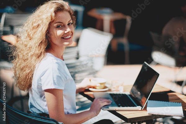 Fototapeta Female student drinking coffee and using laptop while sitting in cafe.