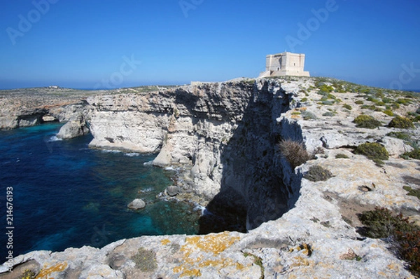Fototapeta Blue lagoon with high cliffs and Santa Marija Tower on Commino Island in Malta (Torri ta' Kemmuna)