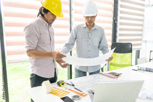 Fototapeta Two engineering men consalting on architect blueprint at office room. Selective focus.